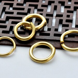May include: Five gold-colored metal jump rings of varying sizes. The rings are smooth and shiny.