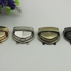 May include: Four metal clasps in different finishes: gold, silver, antique brass, and black. Each clasp has a shield-shaped design with a raised centre.