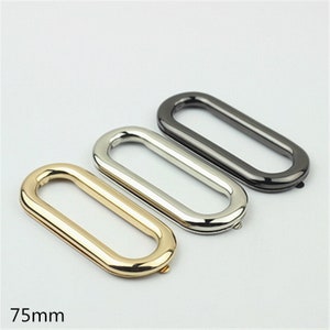 May include: Three oval-shaped metal rings in gold, silver, and black. The rings are approximately 75mm in length. The gold ring is on the bottom left, the silver in the middle, and the black on the top right. The rings are for crafting or hardware.