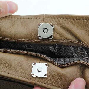 May include: Close-up of a brown leather bag with two silver magnetic closures. The bag has a zippered opening and a patterned lining.