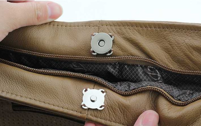 May include: Close-up of a brown leather bag with two silver magnetic closures. The bag has a zippered opening and a patterned lining.