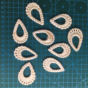 May include: Nine woven teardrop-shaped earrings with a hole at the top for hanging. The earrings are made of natural materials and have a light brown colour.