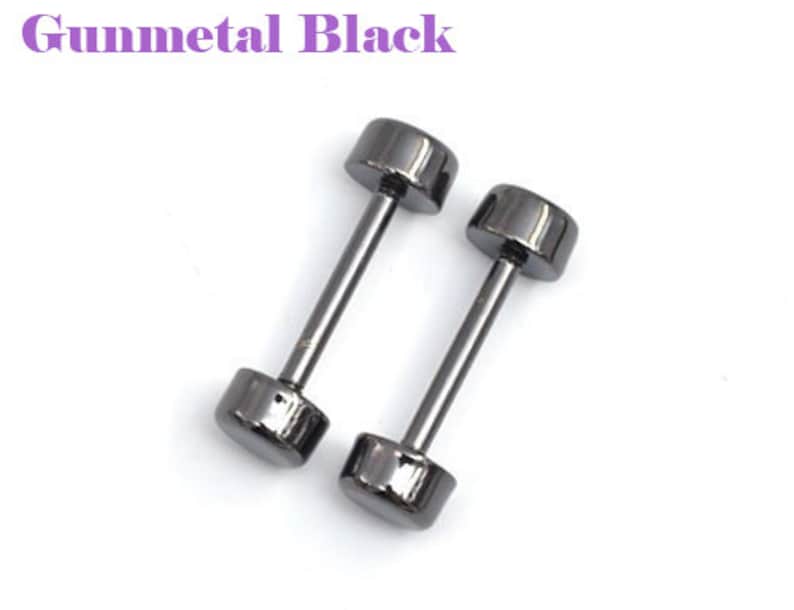 May include: Two gunmetal black dumbbell-shaped earrings. Each earring has a cylindrical post connecting two rounded, flat-topped cylinders. The text "Gunmetal Black" is in the upper left corner. The earrings are set against a white background.