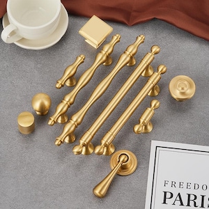 以下が含まれることがあります： 8個の金色のキャビネット金具のプルとノブのセット。プルはさまざまな長さで、シンプルでエレガントなデザインです。ノブは丸く、わずかに盛り上がった中心があります。