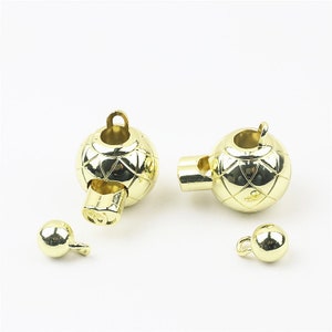 May include: Gold-toned metal clasps for necklaces or bracelets. Each clasp features a round ball with a diamond pattern and a small loop on the side. The clasps are designed to be magnetic.