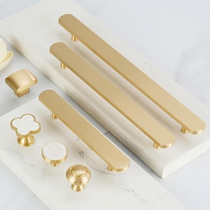 May include: A set of gold cabinet hardware, including pulls and knobs. The pulls are long and rectangular, while the knobs are round and have a variety of designs.