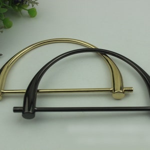 May include: Two metal handbag handles, one gold and one black, with a D-ring shape and a straight bar connecting the ends.
