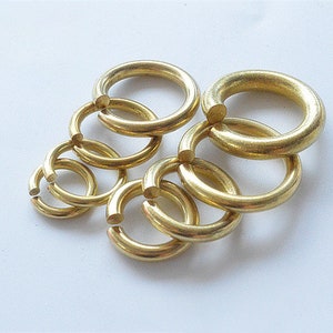 May include: A set of six gold-colored metal jump rings of varying sizes. The rings are interlocked and arranged in a circular pattern.