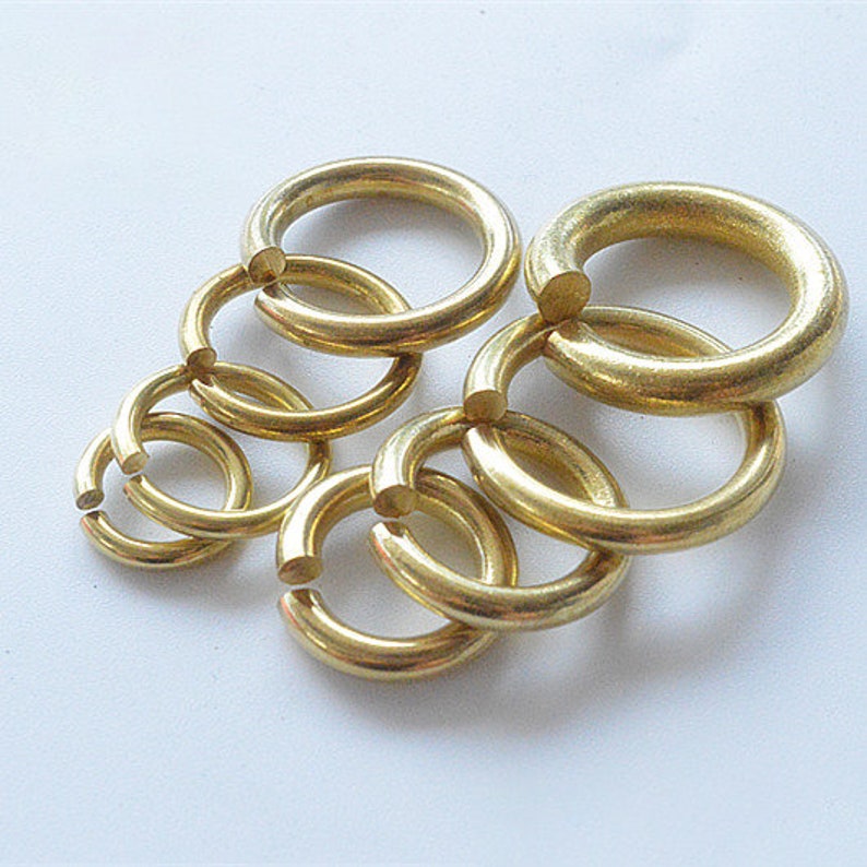 May include: A set of six gold-colored metal jump rings of varying sizes. The rings are interlocked and arranged in a circular pattern.
