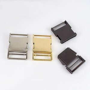 May include: Three metal belt buckles in different finishes: silver, gold, and black. The buckles are all the same size and shape, with a rectangular design.