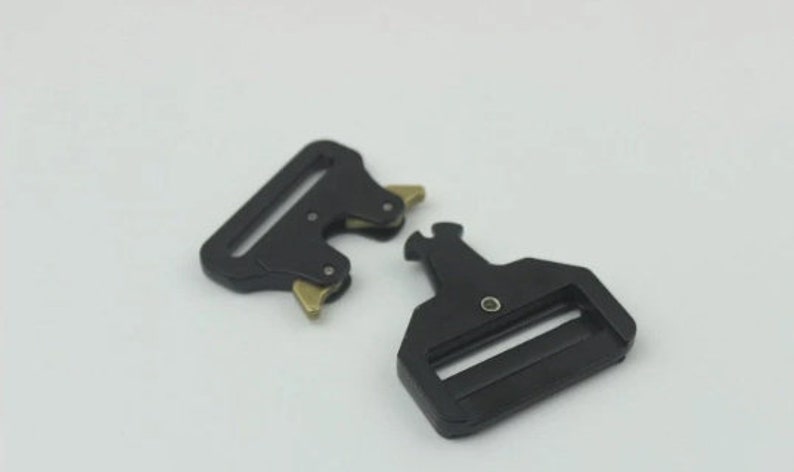May include: Two black metal belt buckle clips with a gold finish. The clips are designed to be used with webbing straps.