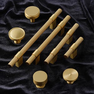 May include: A set of six gold-toned cabinet knobs and pulls with a textured, diamond-shaped pattern. The knobs are round and the pulls are rectangular with a cylindrical shape.