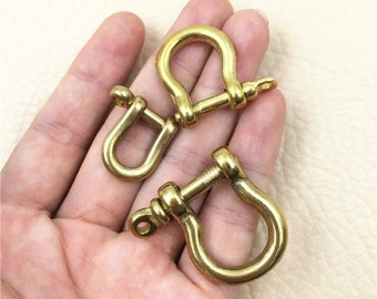 May include: Two gold-colored metal D-rings with a screw-on design. The D-rings are shown in a hand.