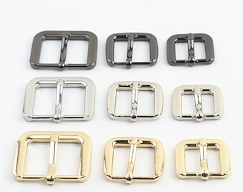 Könnte beinhalten: Sortiment aus Metall-Gürtelschnallen in drei Ausführungen: Schwarz, Silber und Gold. Die Schnallen sind quadratisch mit glatter Oberfläche und in drei Größen erhältlich.