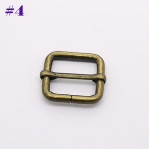 May include: A gold-toned metal buckle with a square shape and a center bar. The buckle is designed for use with straps or belts.