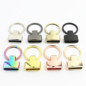 May include: Eight keychains with different colored metal finishes. The keychains have a round ring and a rectangular metal piece with a slot for a key.