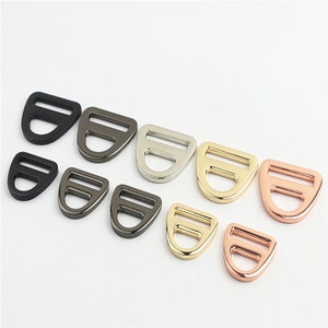 May include: Assortment of metal D-ring buckles in various sizes and finishes, including black, silver, gold, and rose gold.