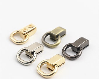 Puede incluir: Cinco cierres de anillo en D de metal en diferentes acabados: dorado, plateado, latón antiguo y negro. Cada cierre tiene una base rectangular con un anillo en forma de D.