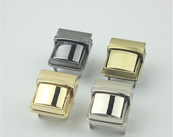 May include: Four metal clasps in different finishes: silver, gold, black, and antique brass. Each clasp has a square shape with a raised, rectangular center piece.