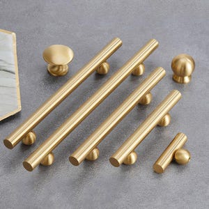 May include: A set of gold-toned cabinet hardware, including knobs and pulls. The knobs are round and the pulls are rectangular with rounded ends. The hardware is made of metal and has a polished finish.