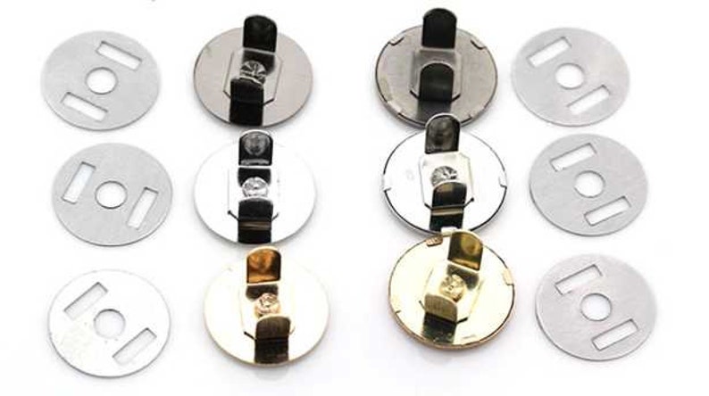 May include: A set of nine magnetic snaps in three finishes: silver, black, and gold. Each snap has a round base with a small hole in the center and a hook-like attachment on the top. The snaps are designed for use in sewing and crafting projects.