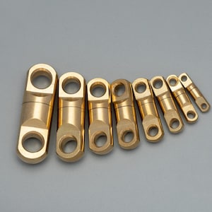 May include: A set of eight brass fishing swivels arranged in a row from largest to smallest. Each swivel features a cylindrical body with a rotating eyelet at both ends, designed for connecting lines and preventing twisting during use.