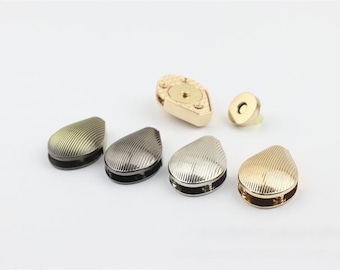 May include: Five teardrop-shaped magnetic closures in gold, silver, and black metal finishes. The closures have a textured, ribbed design. A separate magnetic clasp is also included.