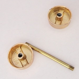 May include: Three gold-colored cabinet knobs with a matching gold-colored screw. The knobs are round with a flat top and a recessed area on the bottom. The screw is long and thin with threads on both ends. The knobs have the number "1156" stamped on them.