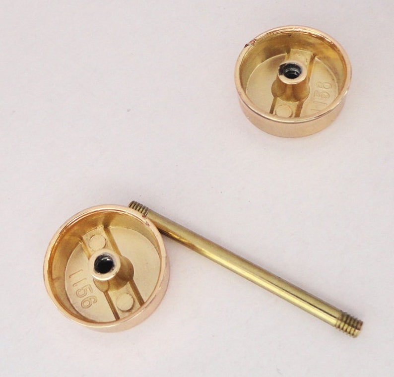 May include: Three gold-colored cabinet knobs with a matching gold-colored screw. The knobs are round with a flat top and a recessed area on the bottom. The screw is long and thin with threads on both ends. The knobs have the number "1156" stamped on them.