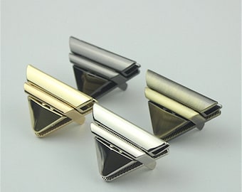 May include: Three metal corner protectors in different finishes: silver, gold, and antique brass. Each protector has a triangular shape with a decorative design.