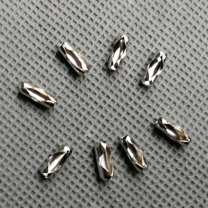May include: Seven silver metal chain links, each with a diamond-shaped pattern, are arranged in a starburst pattern on a gray textured surface.