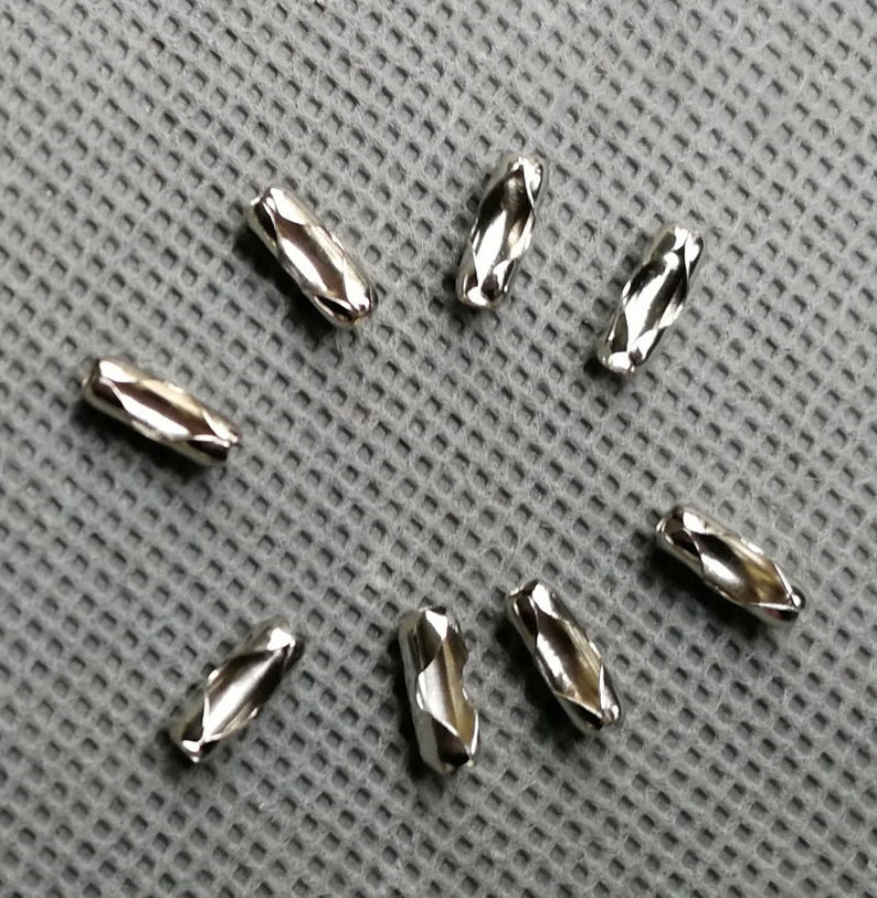 May include: Seven silver metal chain links, each with a diamond-shaped pattern, are arranged in a starburst pattern on a gray textured surface.