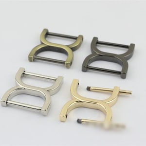 May include: Four metal D-ring buckles in different finishes: gold, silver, antique brass, and black. The buckles are all the same size and shape, with a double D-ring design.