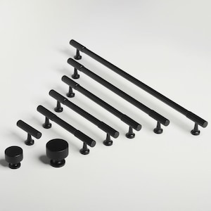 以下が含まれることがあります： さまざまなサイズで、黒色の金属製のキャビネットのプルとノブのセット。プルはリブ付きのデザインで、ノブは丸い形をしています。