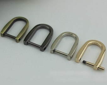 May include: Four metal D-rings in different finishes: antique brass, black, silver, and gold. The rings are all the same size and shape, with a rounded top and a flat bottom.