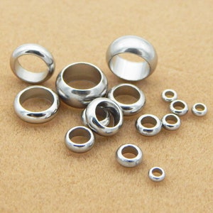 May include: A collection of silver metal rings of various sizes. The rings are smooth and shiny, and they are arranged in a random pattern on a brown surface.