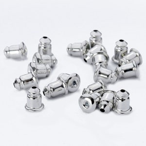 May include: A close-up of a group of silver earring backs. The backs are small and round, with a small hole in the center. They are designed to be used with stud earrings.