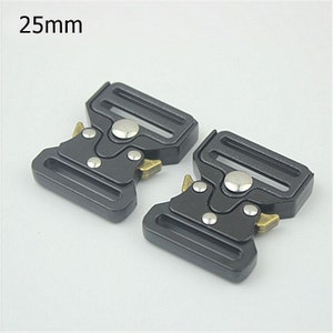 May include: Two black metal belt buckles with silver and gold accents. The buckles are 25mm wide.