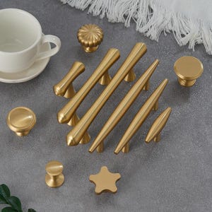 May include: A set of ten gold-toned cabinet knobs and pulls. The knobs are round and the pulls are long and narrow. The knobs and pulls have a brushed finish.