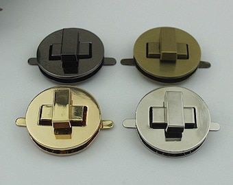 May include: Four metal purse clasps in different finishes: black, antique brass, gold, and silver. Each clasp is round with a rectangular locking mechanism and small tabs on the sides for attachment. These clasps are ideal for handbags and other craft projects.