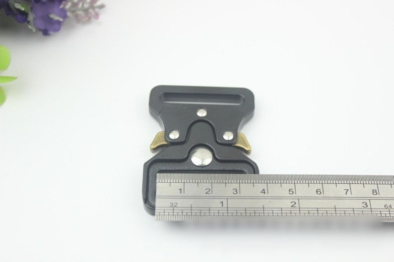 May include: A black metal buckle with gold accents, measuring approximately 1 1/2 inches in length. The buckle is designed for use with webbing or straps.