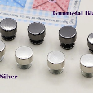 May include: A close-up of eight metal buttons in two colors: silver and gunmetal black. The buttons are round and have a raised center. The buttons are arranged in two rows of four.