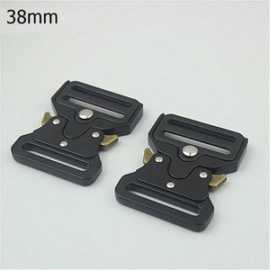May include: Two black metal belt buckle clips with a 38mm width. The buckles have a silver button and gold accents.