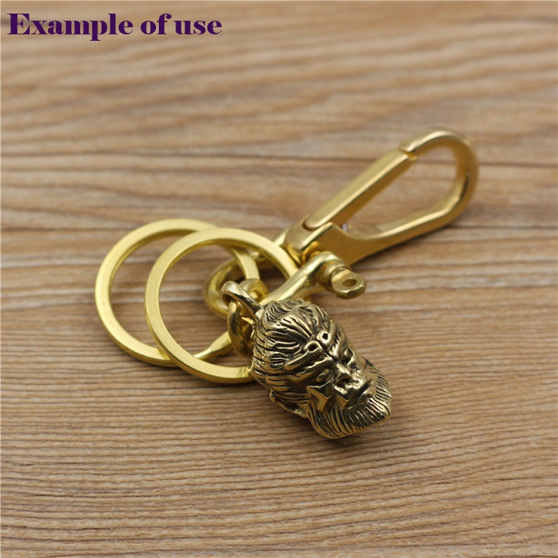 May include: A gold-colored keychain featuring a detailed gorilla head pendant. The keychain includes a split ring and a lobster clasp for easy attachment. The text "Example of use" is in the upper left corner.