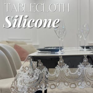 May include: Clear silicone tablecloth with a decorative, scalloped edge featuring intricate white and tan floral embroidery. The text "TABLECLOTH Silicone" is displayed at the top. The table is set with plates and wine glasses.