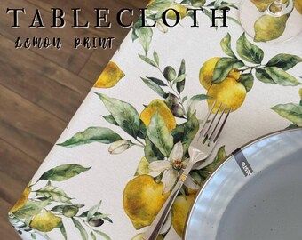 Puede incluir: Un mantel impermeable con estampado de limones. El mantel blanco presenta un patrón repetido de limones amarillos, hojas verdes y flores blancas. Las palabras "WATERPROOF TABLECLOTH LEMON PRINT" están impresas en la esquina superior izquierda.