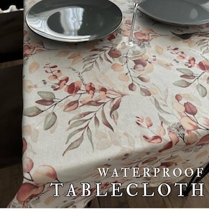 Puede incluir: Un mantel floral impermeable con un diseño botánico en tonos beige, verde y burdeos. El texto "WATERPROOF TABLECLOTH" es visible. Se ven dos platos y una copa de vino.