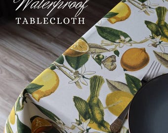 Può includere: Una tovaglia impermeabile bianca con un motivo a limoni e uccelli. Il design presenta limoni gialli, foglie verdi e piccoli uccelli. Le parole "Waterproof TABLECLOTH" sono stampate in bianco.