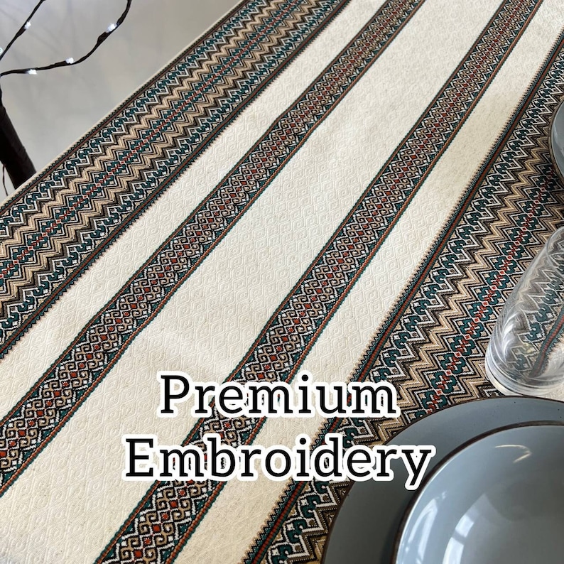 May include: White table runner with three embroidered stripes in brown, green, and beige. The stripes feature geometric patterns. The text "Premium Embroidery" is superimposed on the image.