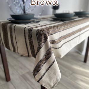 May include: A brown and white striped tablecloth with a geometric pattern. The tablecloth is made of linen and has a rustic look.